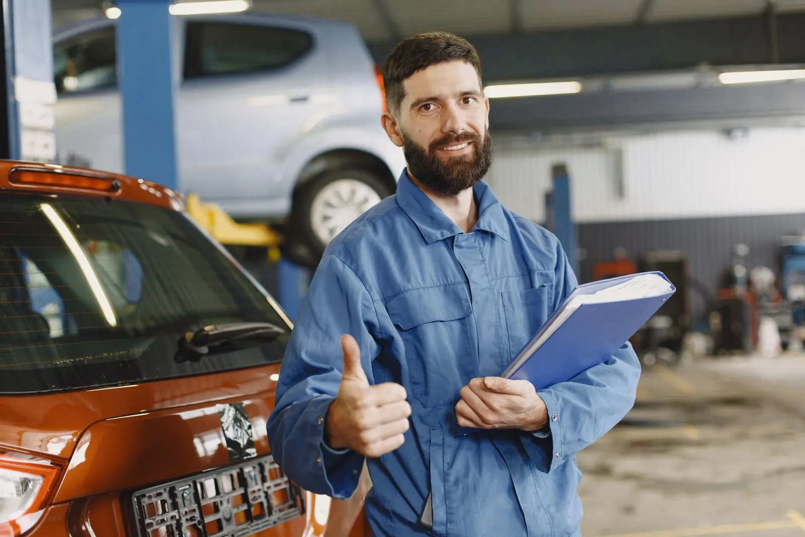 Smiling Autotech technician in blue coveralls giving a thumbs up